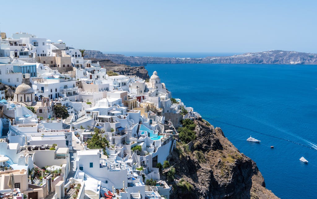 Beautiful Santorini houses overlooking yachts sailing in Greece in the Aegean Sea on a sunny day.