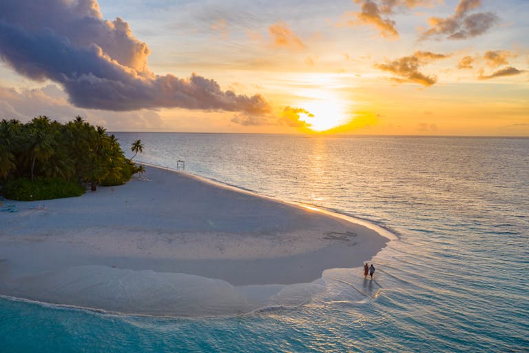 A couple enjoys a serene sunset on a pristine Maldives beach.