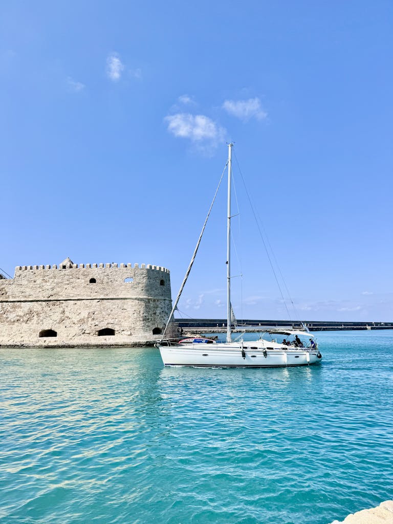 A sailboat gliding past the Venetian Fortress in Heraklion Harbor, Greece on a sunny day.
