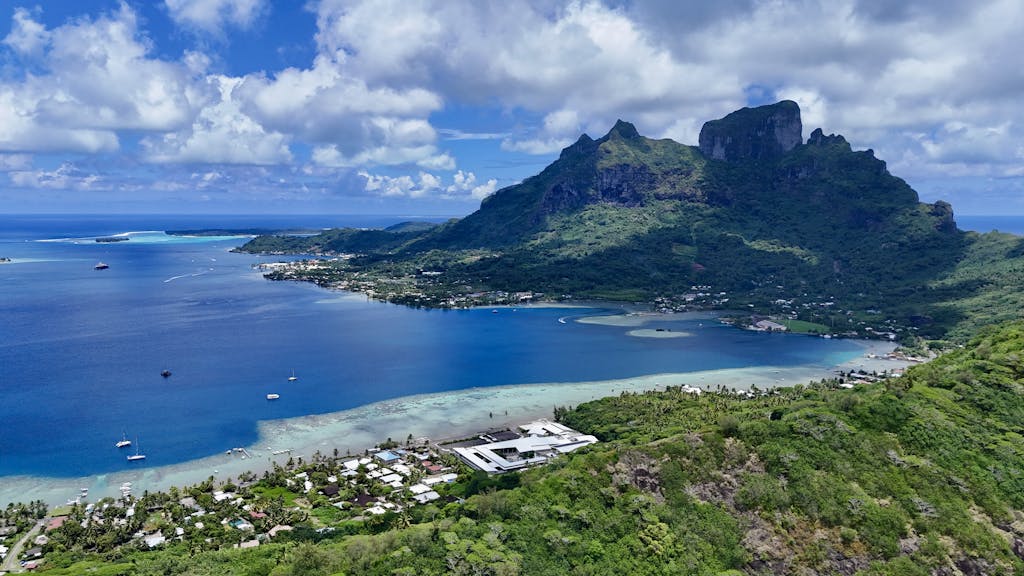 Aerial view of Bora Bora's stunning lagoon and lush mountains under a bright blue sky.