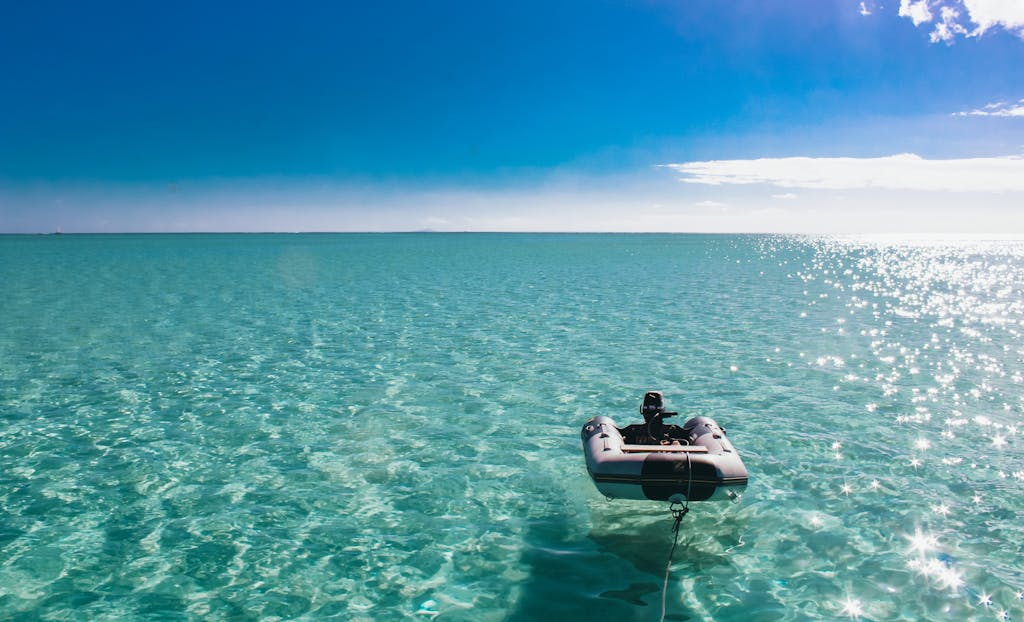 Serene image of a lone inflatable boat floating in the clear turquoise waters of French Polynesia under a bright blue sky.