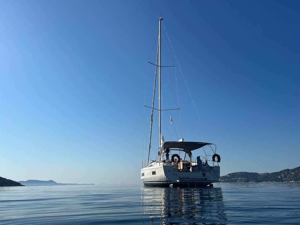 A tranquil scene of a yacht floating on calm water with a clear blue sky in Greece.