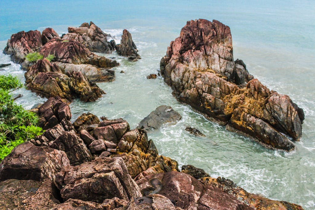A scenic view of the rugged coastline in Koh Chang, Thailand, featuring mossy rocks and vibrant ocean waves.