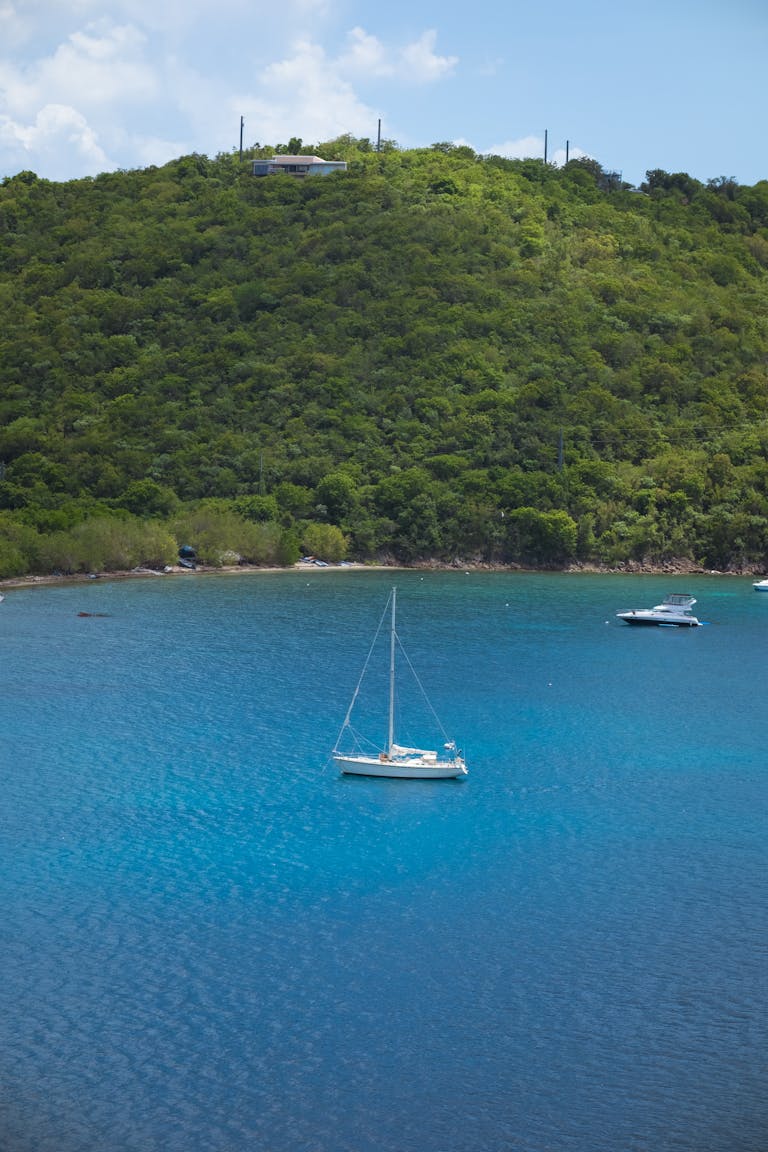 A serene Caribbean bay featuring sailboats on turquoise waters against a lush green hillside backdrop.