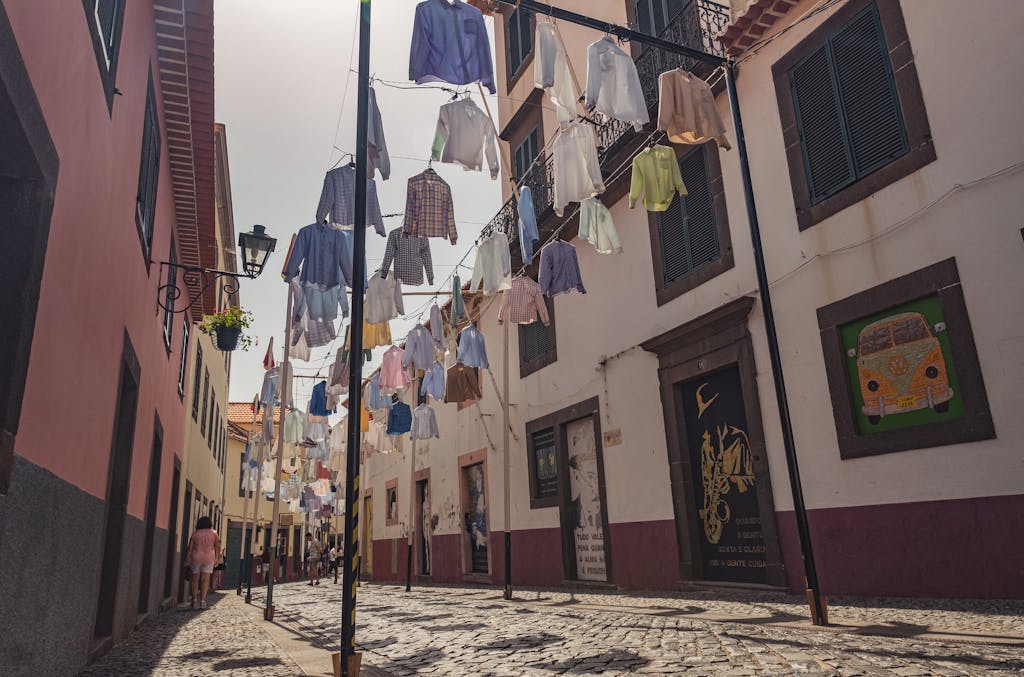 Colorful clothes hung along a charming street in Madeira, Portugal under bright daylight.