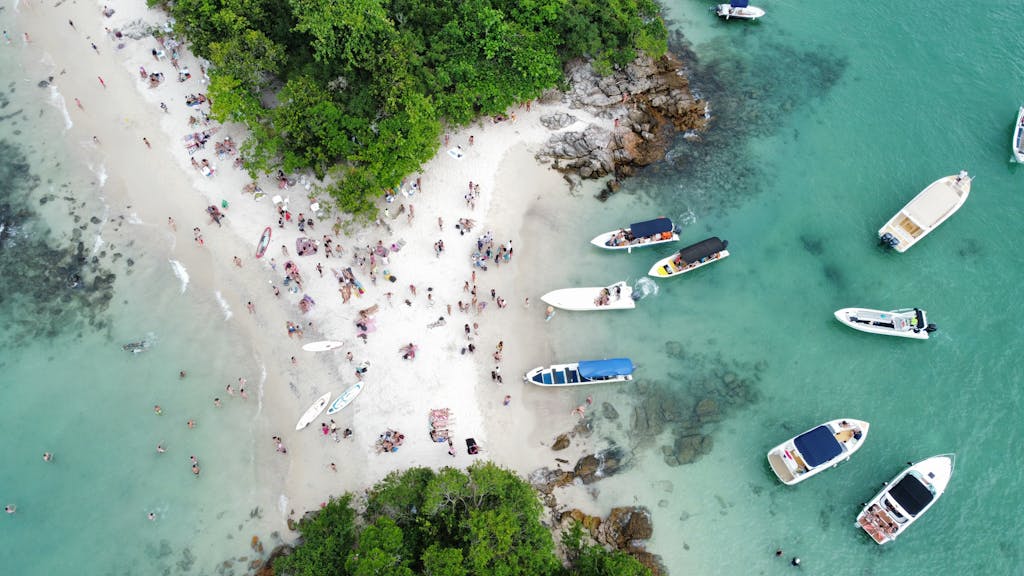 Drone shot of a lively beach in Angra dos Reis, Brazil showcasing people, boats, and lush greenery.
