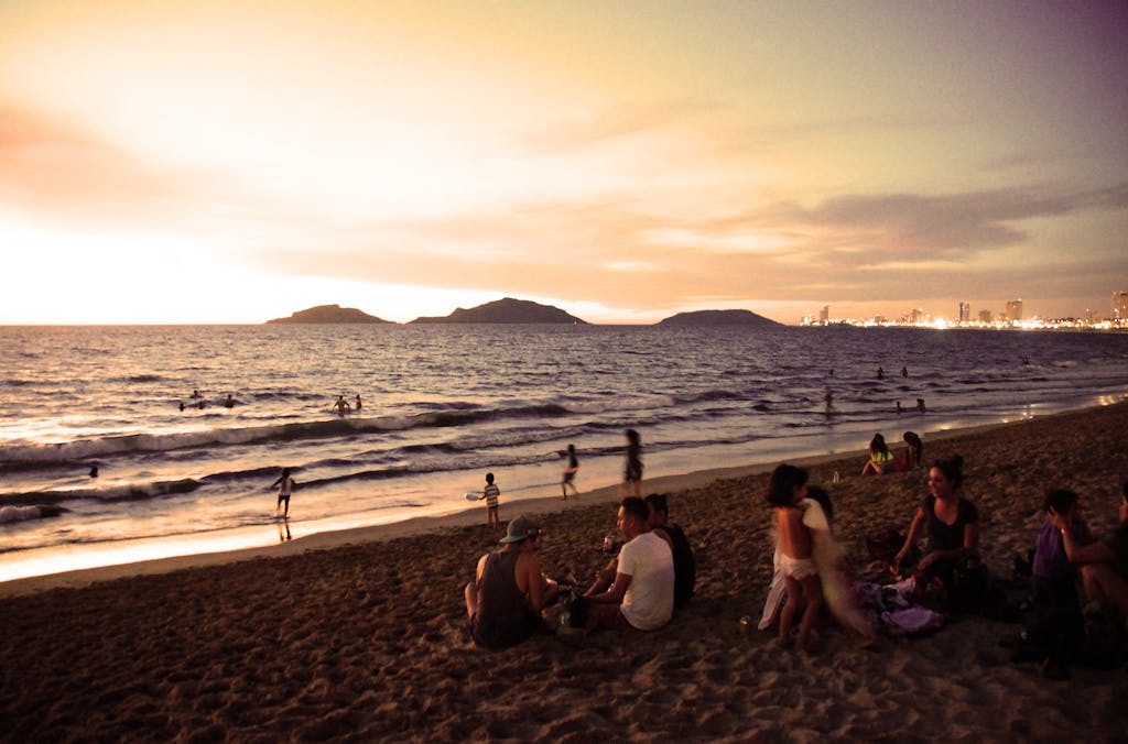 People enjoying the serene sunset at a beach in Mazatlán, with city lights in the distance.