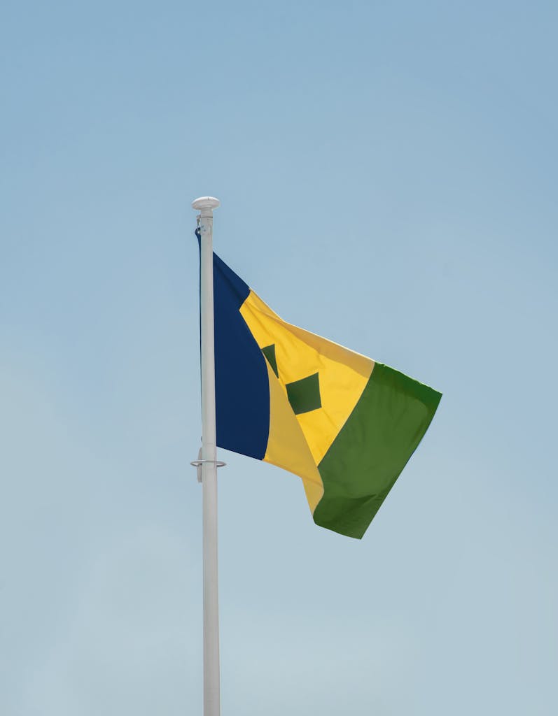 Saint Vincent and the Grenadines flag waving high on a flagpole against a clear blue sky in Kingstown.