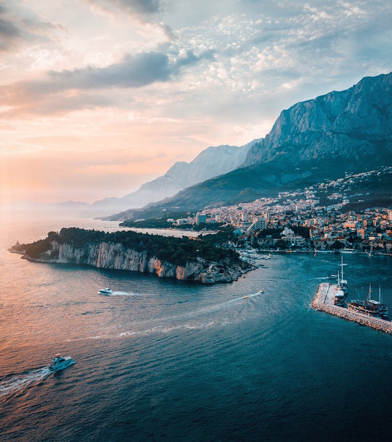 Scenic aerial shot of Makarska, Croatia capturing the coastline, island, and majestic mountains at sunset.