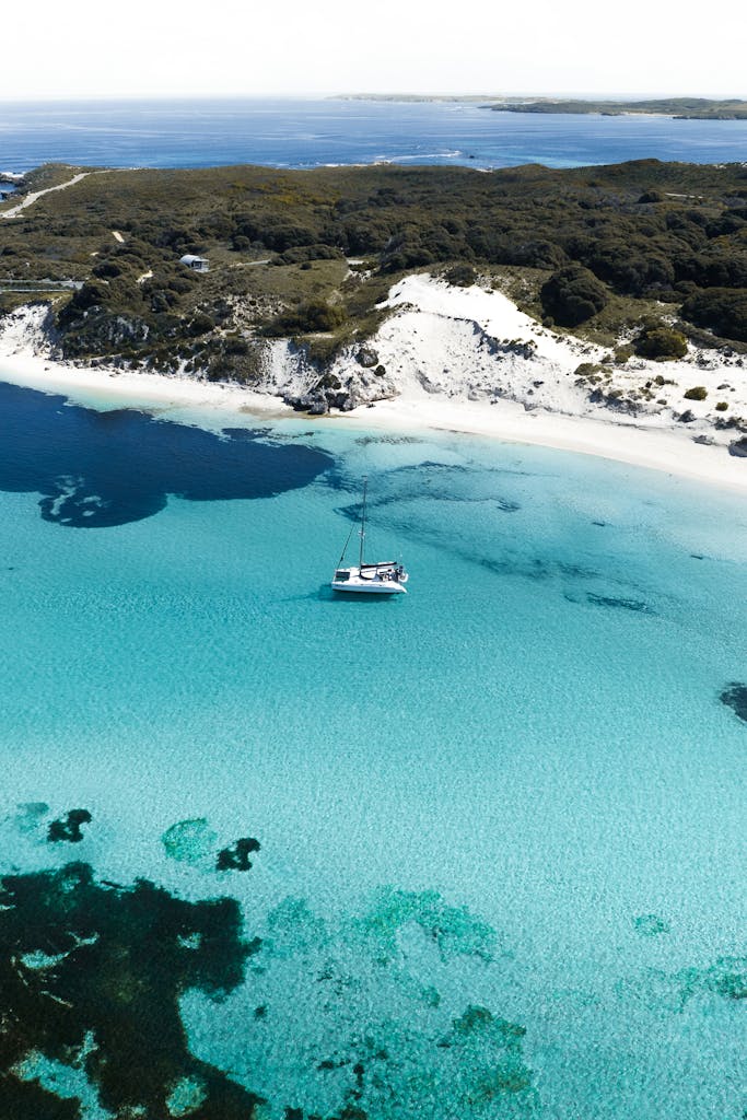Serene aerial view of a yacht anchored near the crystal clear waters of Rottnest Island shore, WA, Australia.