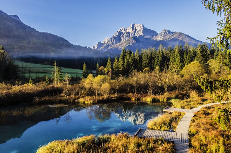 Serene mountain lake with forest reflections and a clear blue sky.