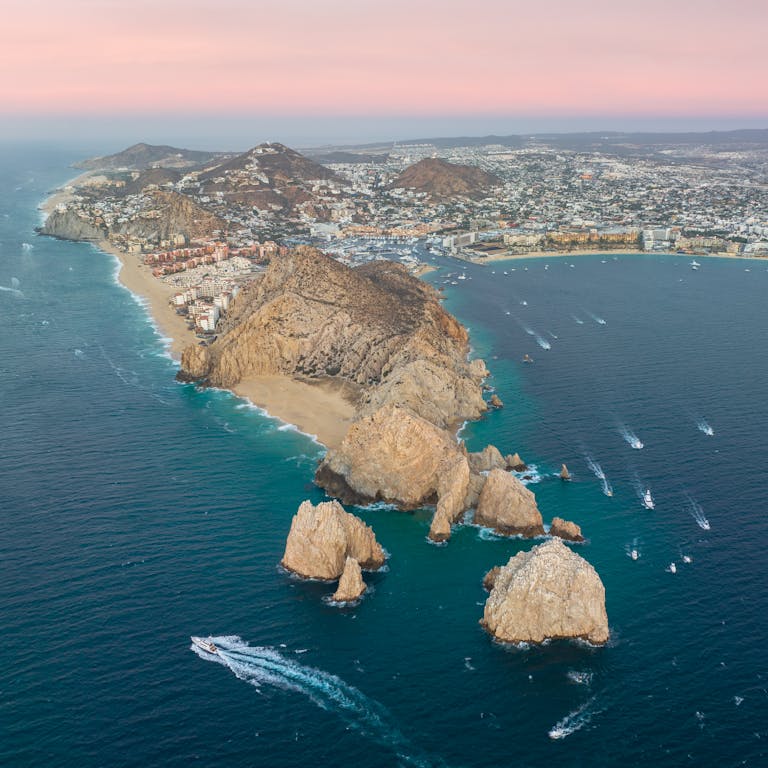 Stunning aerial view of Cabo San Lucas, showcasing the rocky coast and blue sea at sunset.
