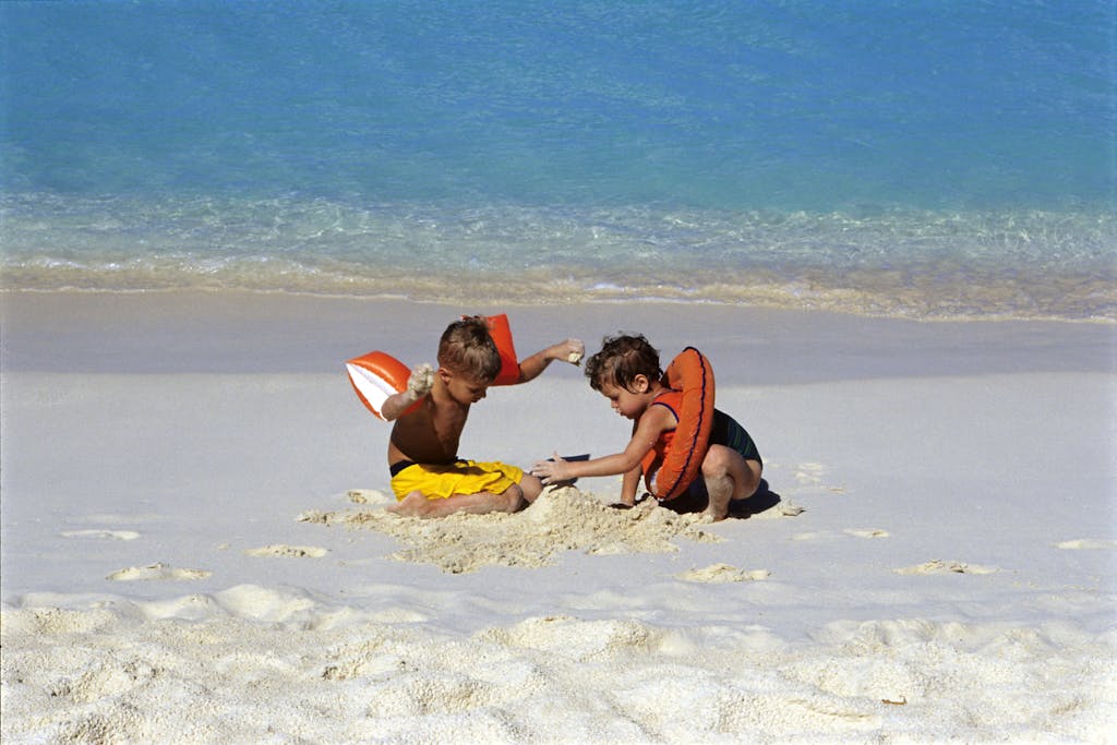 Two kids playing in the sand on a sunny Anguilla beach, wearing floatation devices.