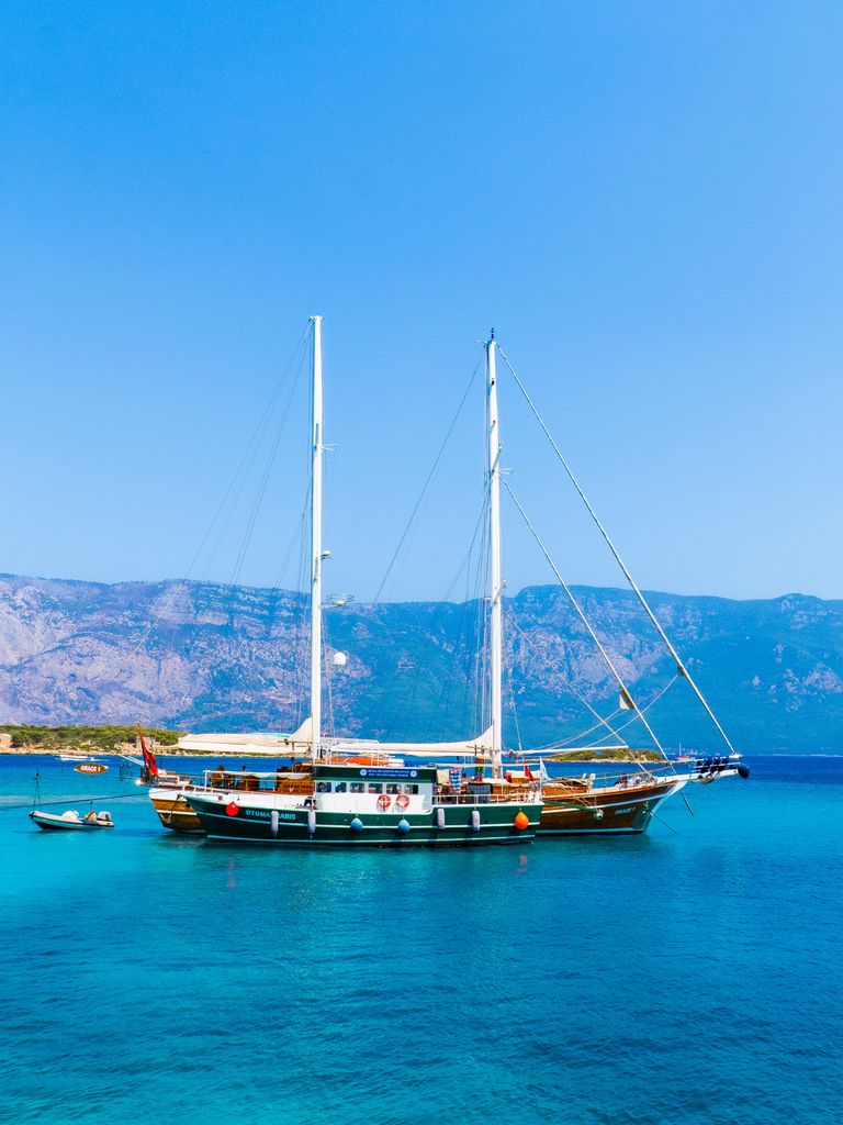 A serene view of a sailing boat on clear blue waters with mountains in the background.